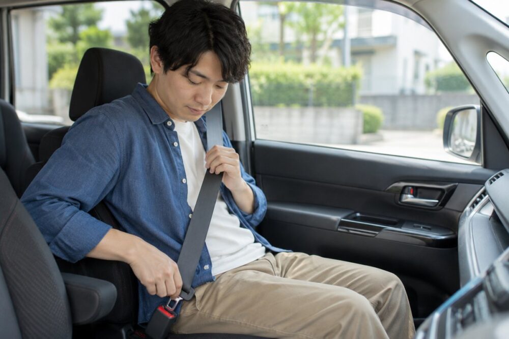 停車中の車内でシートベルトを着ける成人男性のイメージ