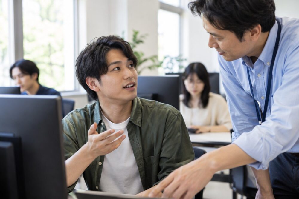 パソコンの前で支援者に質問する成人男性のイメージ